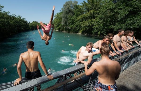 Eine Gruppe von Menschen in Badekleidung springen von einer Brücke in die Aare.