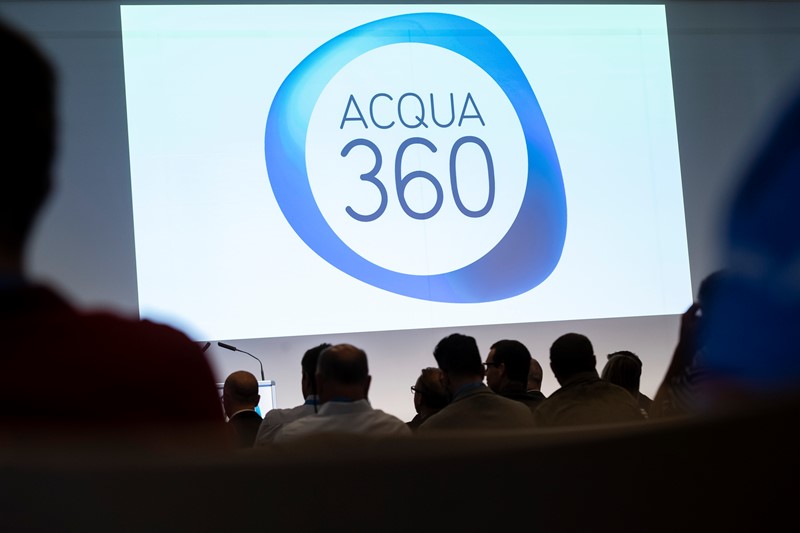 Eine Gruppe von Menschen schaut sich eine Projektion des Acqua 360-Logos an.