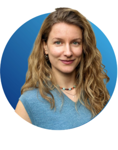 Frau mit langem gewelltem blondem Haar, die ein blaues &auml;rmelloses Oberteil und eine Perlenkette tr&auml;gt, posiert vor einem blauen runden Hintergrund.