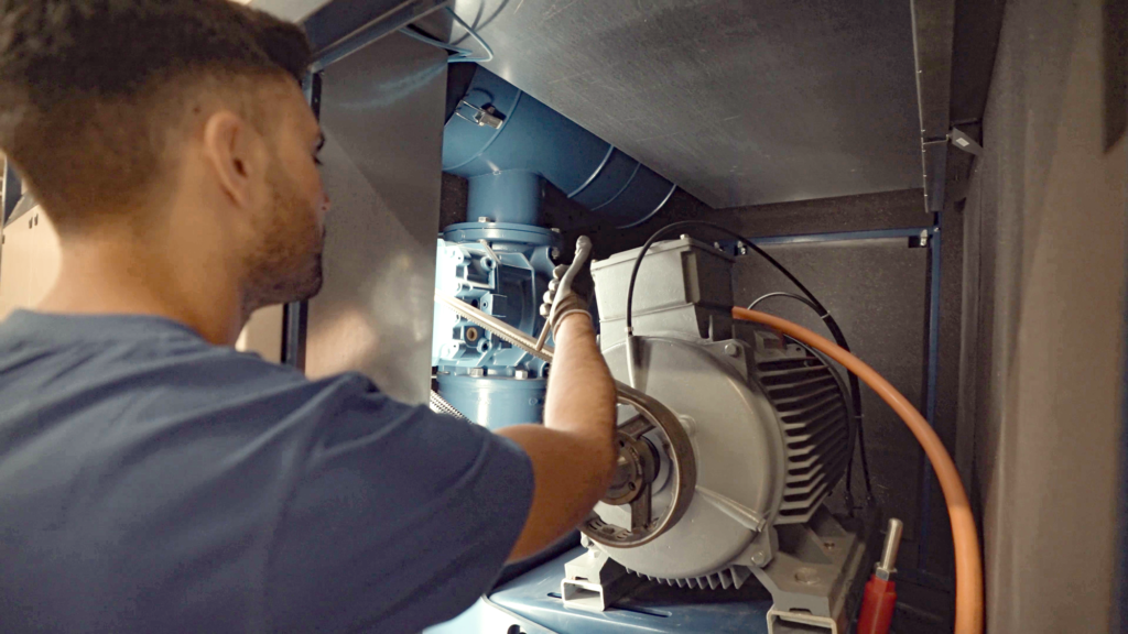 Eine Person im blauen Hemd prüft und justiert Maschinen in einem Schaltschrank für Industrieanlagen.