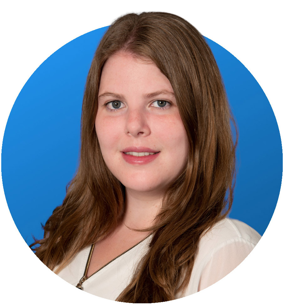 Eine Frau mit langen braunen Haaren, die ein weißes Oberteil und eine Halskette trägt, posiert vor einem einfarbig blauen Hintergrund auf einem kreisförmig zugeschnittenen Porträtfoto.