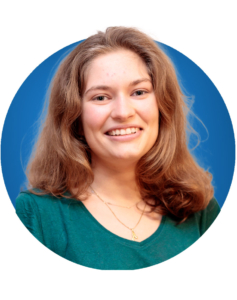 Eine Person mit langen braunen Haaren und einem gr&uuml;nen Oberteil l&auml;chelt vor einem blauen Hintergrund in die Kamera.